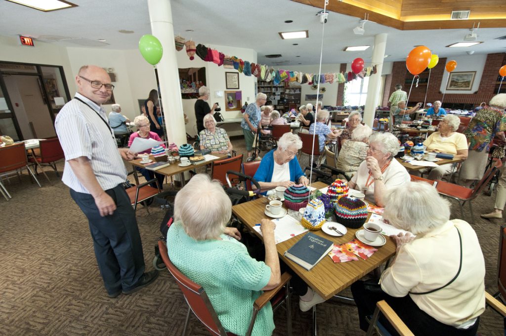 A photo of a elderly get together inside Harmony Hall. Elderly ladies are conversating with each other.