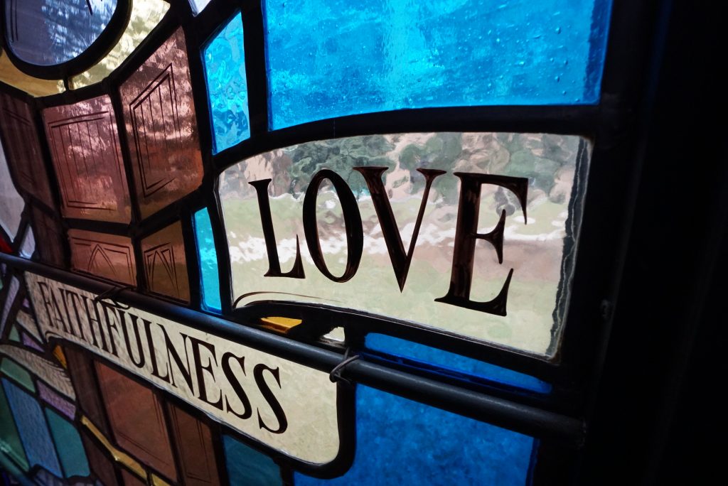 A picture of a coloured glass window inside Heritage Hall that contains the words Love and Faithfulness.