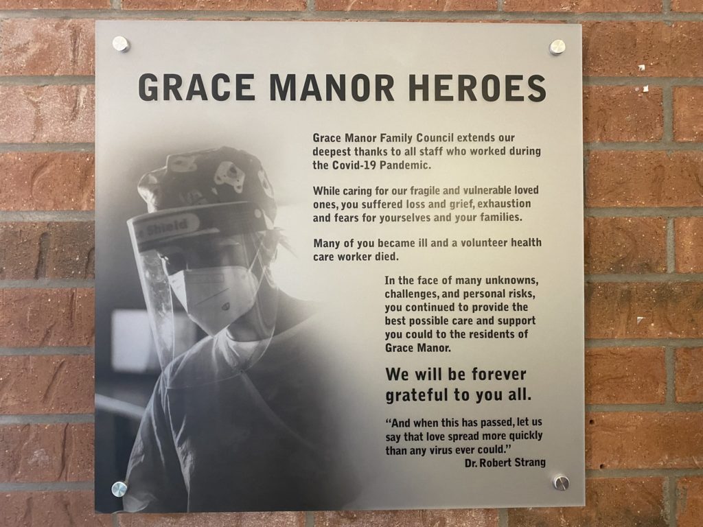 A picture of a sign on a brick wall in Grace Manor that reads "GRACE MANOR HEROES." This sign details Grace Manor's mission to providing good care to it's residents.